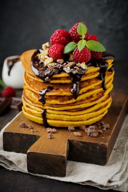 Frittelle di zucca con lamponi freschi, cioccolato e noci su pietra scura o tavolo di cemento.