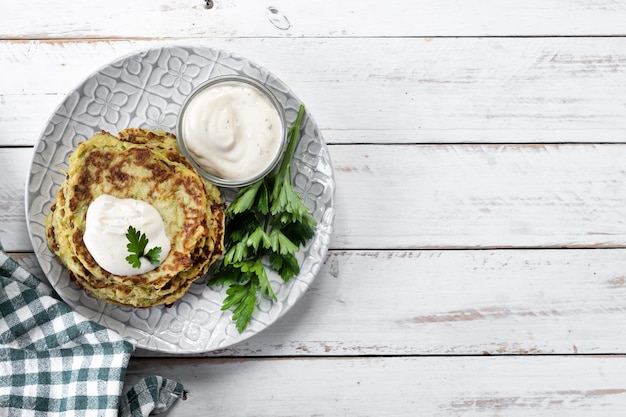 Frittelle di zucchine con salsa allo yogurt sul tavolo di legno bianco