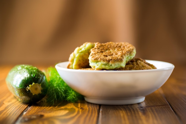 frittelle di zucchine fritte con erbe aromatiche in un piatto su un tavolo di legno