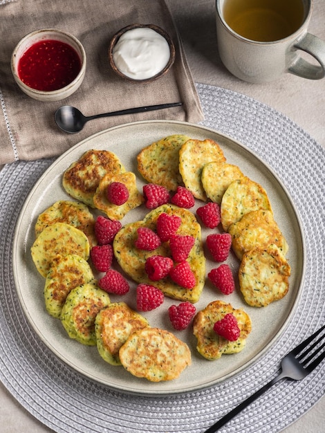 Frittelle di zucchine senza glutine con lamponi freschi, marmellata di lamponi, panna acida su un piatto grigio