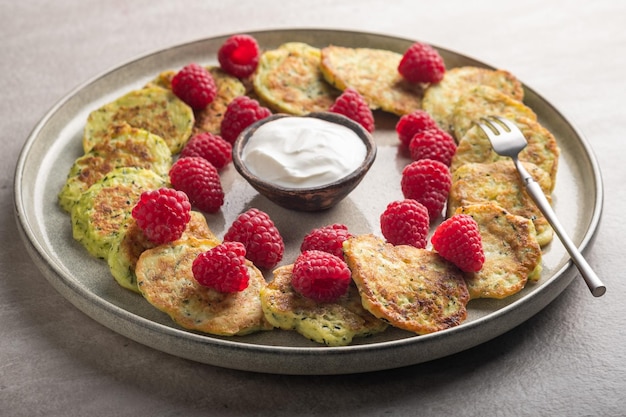 Frittelle di zucchine senza glutine con lamponi freschi, marmellata di lamponi, panna acida su un piatto grigio