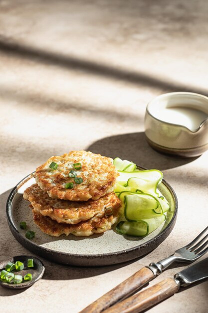 Frittelle di zucchine vegetariane con cetriolo cipolla verde e salsa di panna con ombre in condizioni di luce intensa Spazio di testo