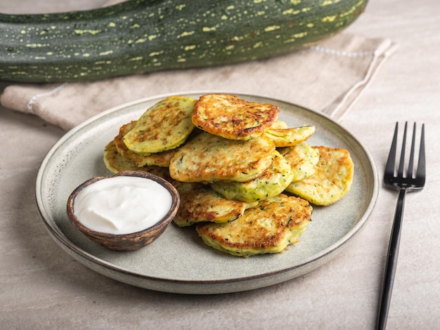 Frittelle di zucchine vegetariane con panna acida su un piatto rotondo e zucchine verdi