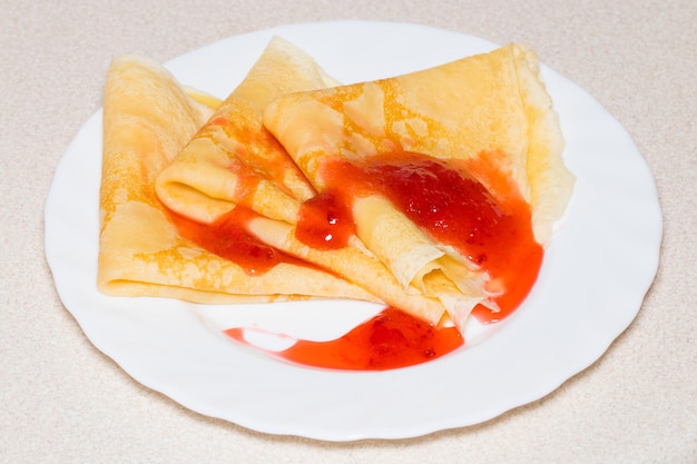 Frittelle dolci con marmellata di fragole su un piatto bianco.