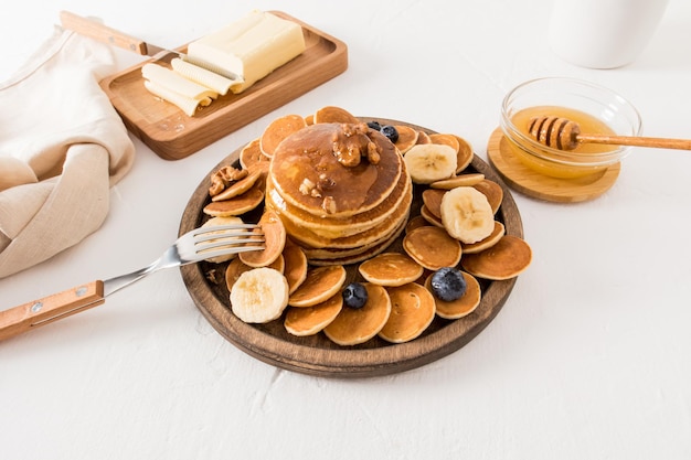 Frittelle fatte in casa con noci di miele e frutti di bosco su un piatto di legno su un tavolo bianco il concetto di uno spuntino sano per la colazione