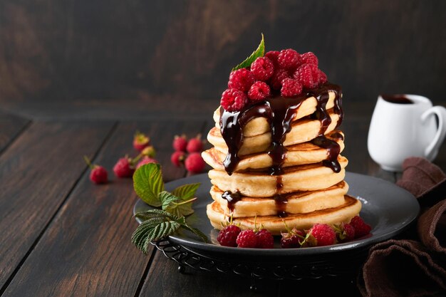 Frittelle Frittelle con lampone fresco con glassa al cioccolato o condimenti in una ciotola grigia sul vecchio tavolo di legno sullo sfondo Frittelle americane classiche fatte in casa Pagina per il concetto di rivista