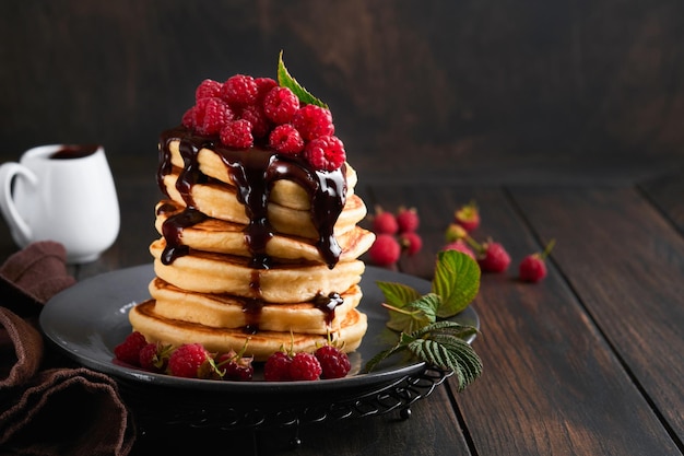 Frittelle Frittelle con lampone fresco con glassa al cioccolato o condimenti in una ciotola grigia sul vecchio tavolo di legno sullo sfondo Frittelle americane classiche fatte in casa Pagina per il concetto di rivista