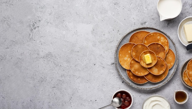 Frittelle piatte servite su sfondo grigio cemento con marmellata di burro panna acida latte e miele Ampio banner con spazio per la copia Vista dall'alto