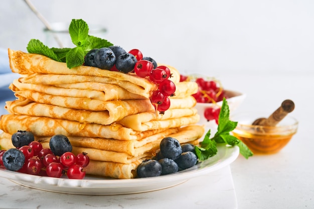 Frittelle Pila di crepes o frittelle sottili con frutti di bosco mirtilli ribes rosso lamponi e miele per colazione Colazione fatta in casa Spazio di copia Messa a fuoco selettiva