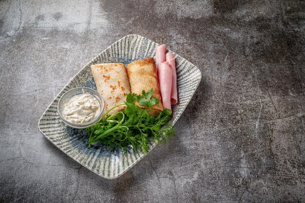 Frittelle ripiene di prosciutto in un piatto con prezzemolo e aneto e panna acida su una tavola di pietra grigia, flatlay