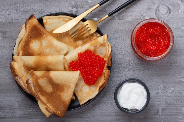 Frittelle russe con caviale rosso su un tavolo grigio