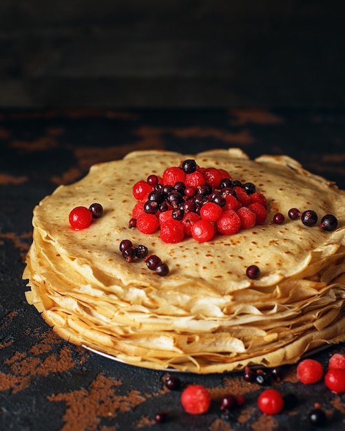 Frittelle russe con frutti di bosco davanti a uno sfondo scuro. Settimana del pancake