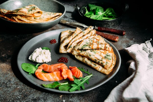 Frittelle sottili con erbe aromatiche, salmone e crema di formaggio su un piatto