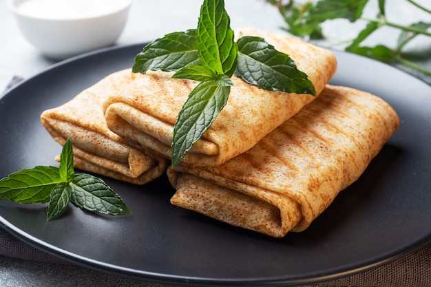 Frittelle sottili ripiene su un piatto nero con menta