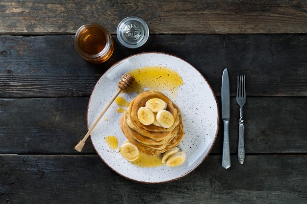 frittelle sul piatto in ceramica servito con banane e miele su legno