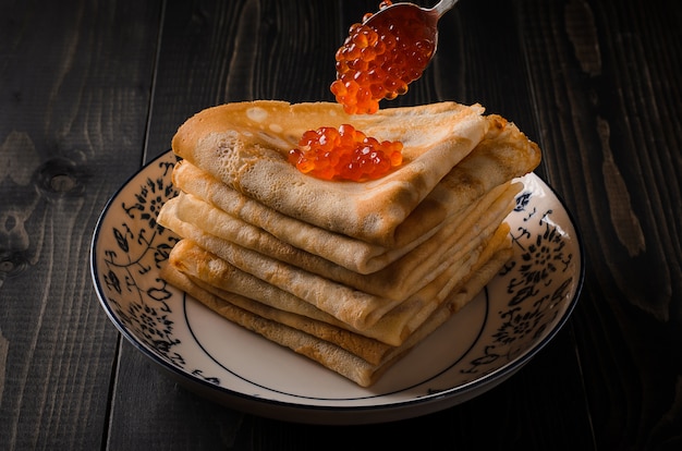 Frittelle tradizionali russe con caviale rosso con un cucchiaino di caviale rosso d&#39;argento sono poste su una pila di pancake.