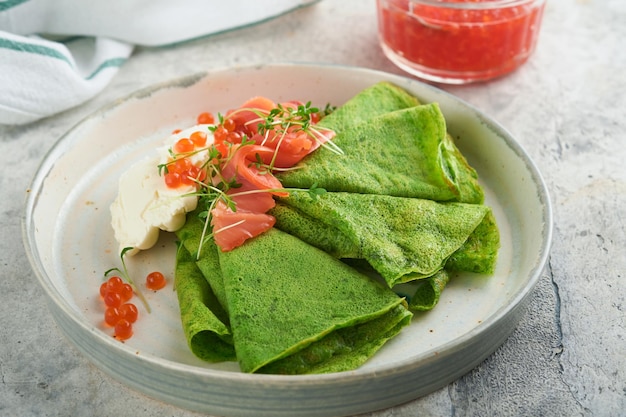 Frittelle verdi Frittelle rotonde sottili di crepe di spinaci verdi con caviale rosso e nero e salsa allo yogurt su sfondo grigio cemento Colazione vegana sana Giornata nazionale delle frittelle o giorno del martedì grasso