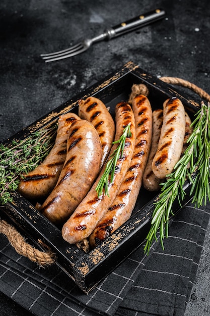 Fritto su una padella alla griglia, mescolare le salsicce in un vassoio di legno con erbe aromatiche Sfondo nero Vista dall'alto