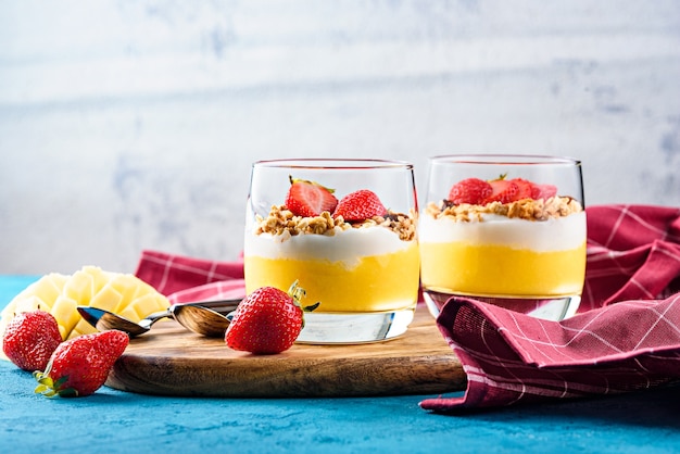 Frontali due coppe di vetro con dessert di frutta e bacche di mango e fragole con muesli e crema alla vaniglia o ricotta