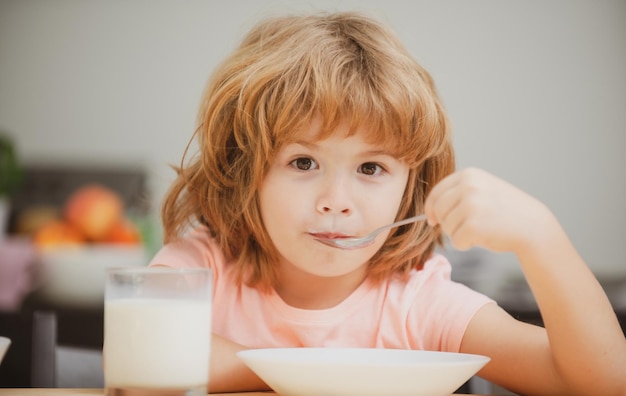 Fronte del primo piano del bambino che mangia cibo biologico, yogurt, latte. Il bambino mangia sano. Ragazzino sorridente che mangia cibo in cucina.