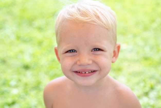 Fronte del primo piano del bambino sorridente sveglio della sorgente. Concetto di emozioni del bambino. Ritratto di giovane ragazzo che ride all'aperto.