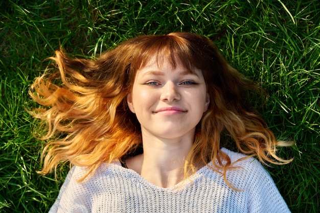 Fronte del primo piano della femmina adolescente rossa felice sulla vista superiore del fondo erboso