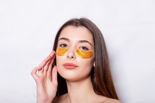 Fronte Di Bellezza Della Donna Con La Maschera Sotto Gli Occhi. Bella femmina con trucco naturale e patch di collagene d'oro sulla pelle del viso fresca. Alta risoluzione