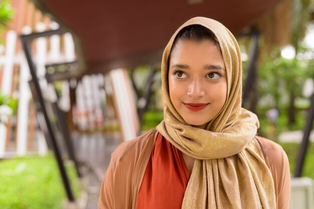 Fronte di giovane bella donna musulmana indiana che pensa nella città con la natura