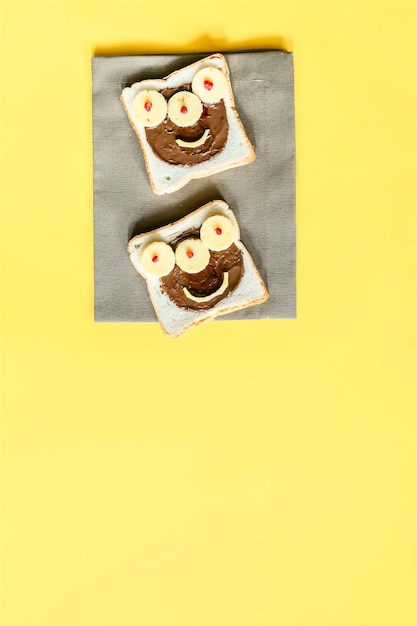 Fronte divertente del mostro sul pane tostato del panino di Halloween con il burro di arachidi, formaggio sul fondo giallo del tovagliolo da vicino. Bambini bambino dolce dessert colazione pranzo cibo.