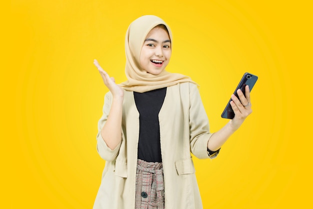 Fronte felice di giovane donna asiatica con lo smartphone sulla parete gialla