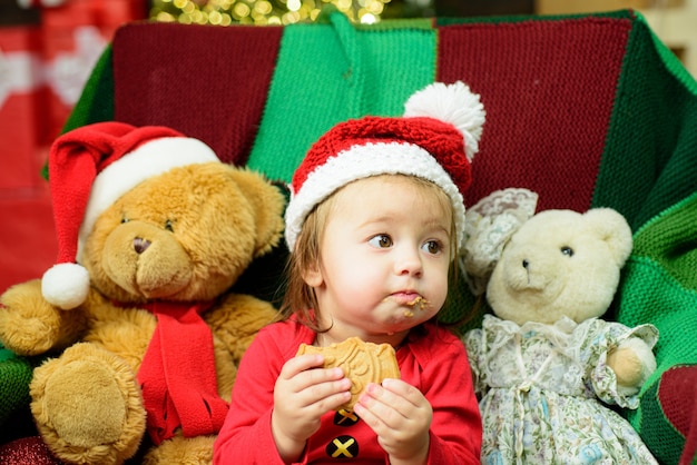 Fronte sveglio del bambino in cappello della Santa vicino all'albero di Natale. Infanzia felice.