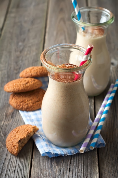 Frullati alla vaniglia di latte con biscotti di farina d'avena in barattoli di vetro sulla vecchia superficie di legno. Messa a fuoco selettiva.