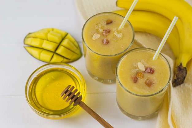 Frullati appena fatti con mango, banana, miele, noci e cereali su un tavolo di legno bianco