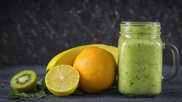 Frullati di avocado, banane, kiwi ed erbe su un tavolo scuro in legno nero