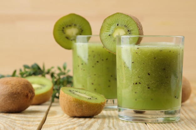 Frullati di kiwi in un bicchiere accanto a fette di kiwi freschi su un tavolo di legno naturale.