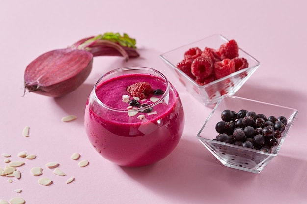 Frullati vegetariani sani di bacche rosse e barbabietola con piatti di mandorle in una tazza di vetro su uno sfondo di carta rosa.