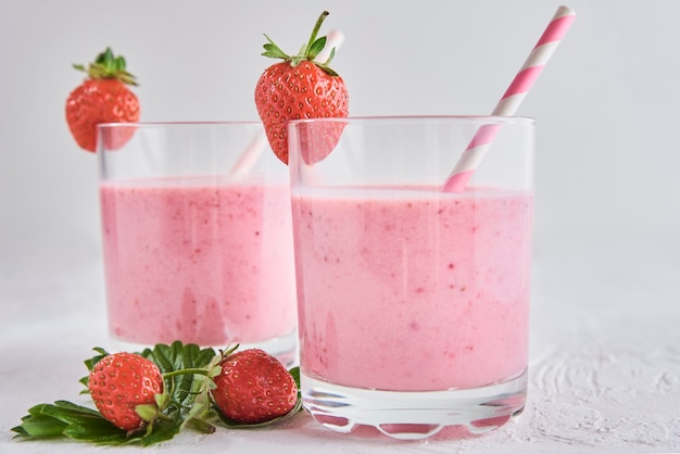 Frullato alla fragola in vetro con paglia e frutti di bosco freschi su sfondo bianco