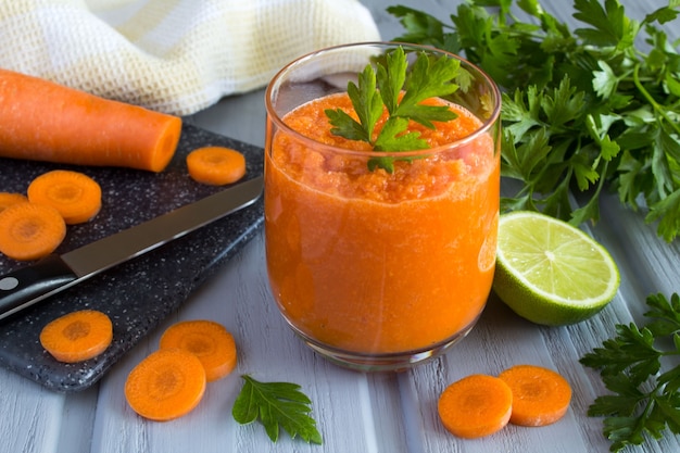 Frullato con carote e ingredienti su fondo di legno grigio