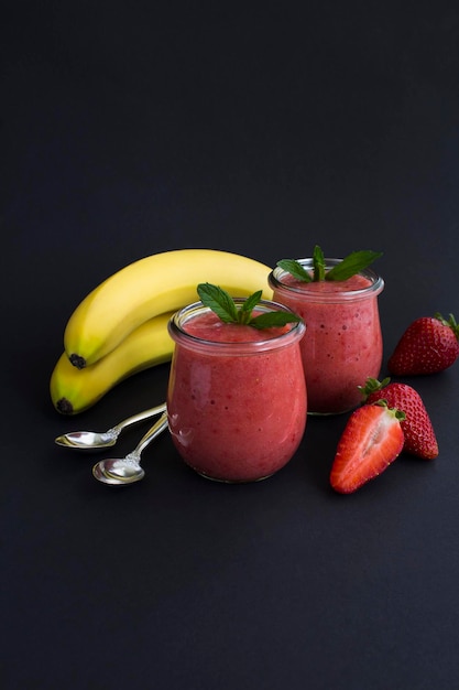 Frullato con fragola e banana nel barattolo di vetro su sfondo nero Spazio di copia Posizione verticale