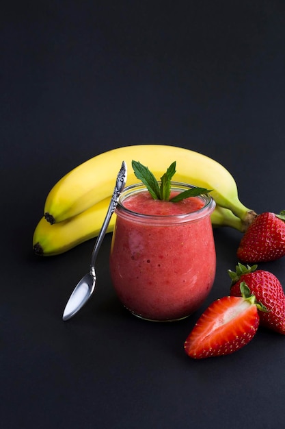 Frullato con fragola e banana nel barattolo di vetro su sfondo nero Spazio di copia Posizione verticale