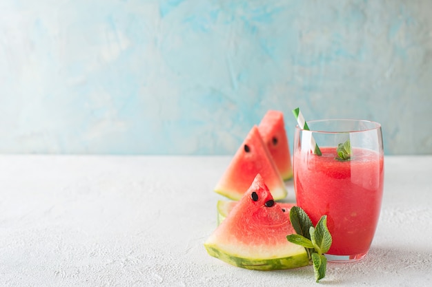 Frullato di anguria con fetta di frutta e foglia di menta su struttura blu e bianca