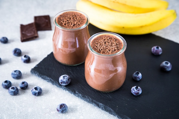 Frullato di banana al cioccolato con semi di chia e mirtillo su uno sfondo di ardesia e pietra.