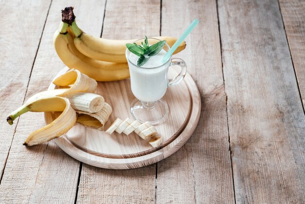 Frullato di banana al latte decorato con foglie di menta in un bicchiere di latte con manico sul tavolo in legno scuro con spazio di copia