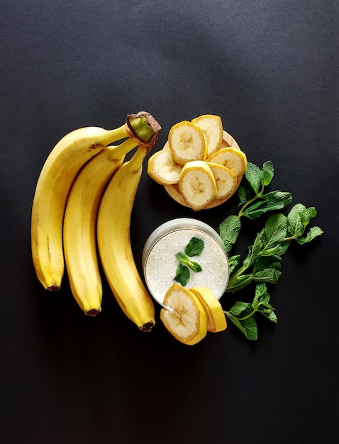 Frullato di banana con un rametto di menta un mazzo di banane e fette di banana su uno sfondo scuro