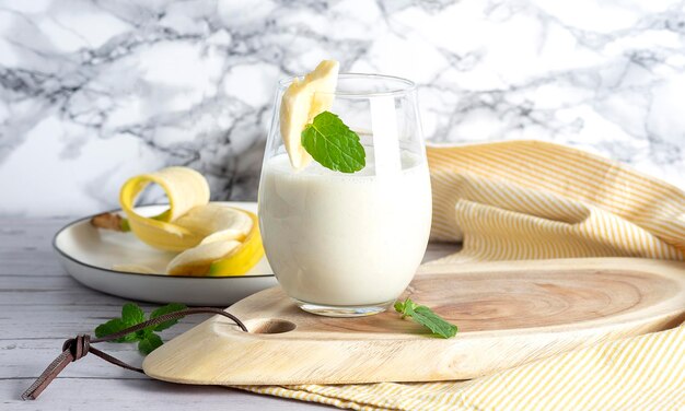 Frullato di banana vegano in tazza di vetro su tavola di legno su sfondo chiaro Cibo sano