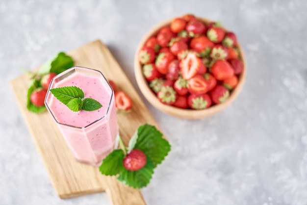 Frullato di fragole in barattolo di vetro e fragole fresche in ciotola di legno su un tagliere