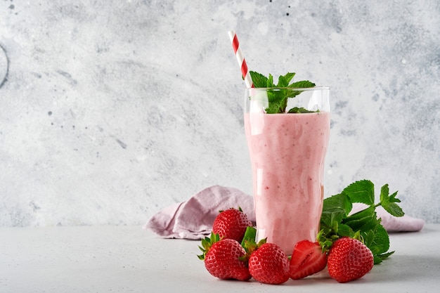 Frullato di fragole o frullato con frutti di bosco e menta in un bicchiere alto su sfondo grigio chiaro. Bevanda estiva shake, milkshake e concetto organico di rinfresco. Posto per il testo.