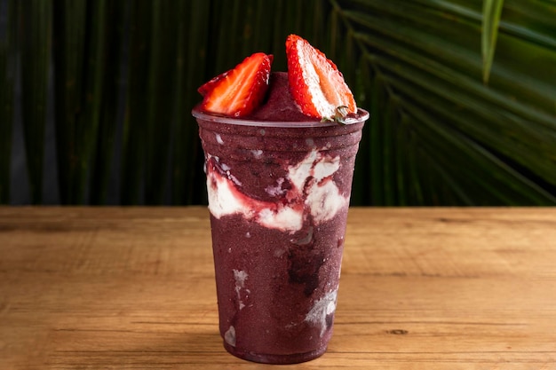 Frullato di gelato alla bacca di AÃ§ai congelato brasiliano in tazza di plastica con fragole, banane e latte condensato. Sullo sfondo di foglie d'estate. Vista frontale per menu e social media