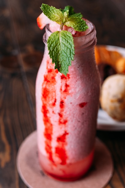 Frullato di yogurt alla fragola in vetro bottiglia rabbocco con foglie di menta.