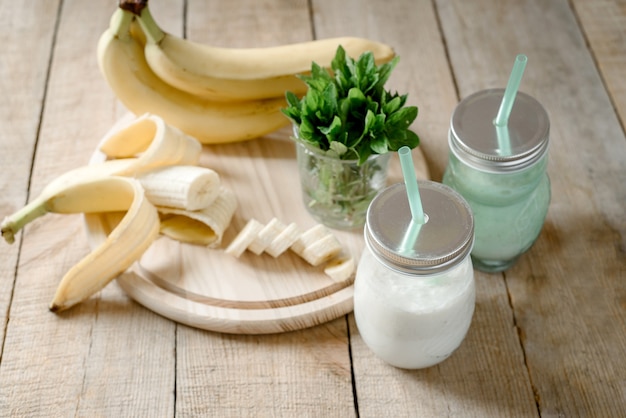 Frullato estivo di banana o frullato con menta e paglia in barattoli su tavola di legno scuro con spazio per le copie